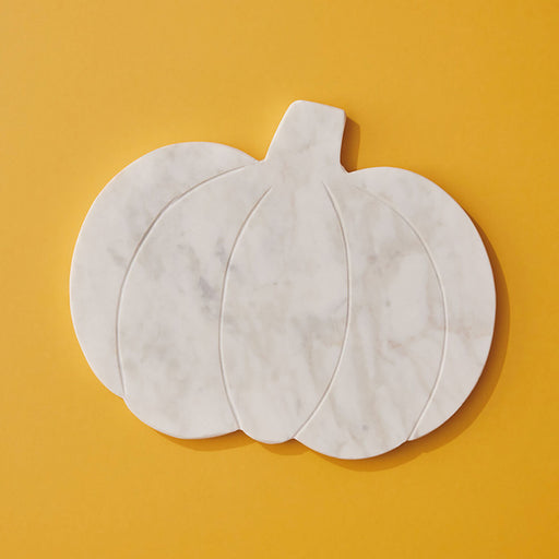 A pumpkin-shaped white marble serving board with a stem, photographed from above on a solid mustard yellow background.