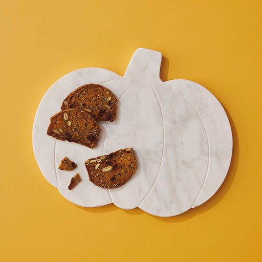 A pumpkin-shaped white marble serving board with decorative baked cookie slices, photographed from above on a solid mustard yellow background.