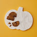 A pumpkin-shaped white marble serving board with decorative baked cookie slices, photographed from above on a solid mustard yellow background.