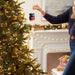 Person decorating a Christmas tree with a 'MOM' ornament in a festive living room.