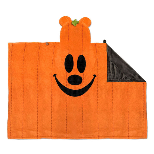 An orange plush blanket shaped like a pumpkin with a stitched vertical paneled design, a black embroidered face, and a folded-over corner revealing a dark gray underside.