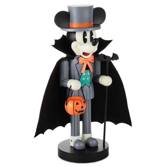 A Mickey Mouse Halloween nutcracker figurine dressed as a vampire, wearing a black top hat with an orange band, a black cape, a gray pinstripe suit, an orange bow tie, and holding an orange jack-o'-lantern bucket, shown on a plain white background.