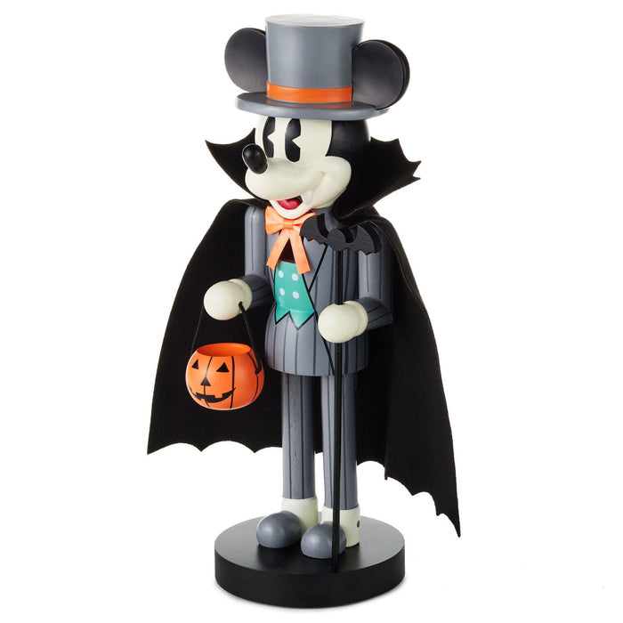 A Mickey Mouse Halloween nutcracker figurine dressed as a vampire, wearing a black top hat with an orange band, a black cape, a gray pinstripe suit, and holding an orange jack-o'-lantern bucket, set against a plain white background.