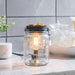 Glass jar with a lit candle inside on a kitchen counter