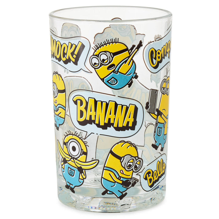 A clear glass tumbler featuring a repeating cartoon Minion print with speech bubbles and bold text including 'BANANA' and 'COMEDY', shown on a plain white background.