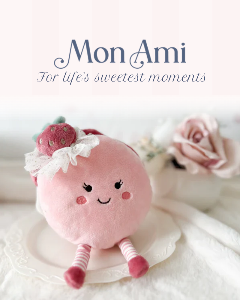 Pink plush toy with a bow and flowers, branded 'Mon Ami', on a soft white background.