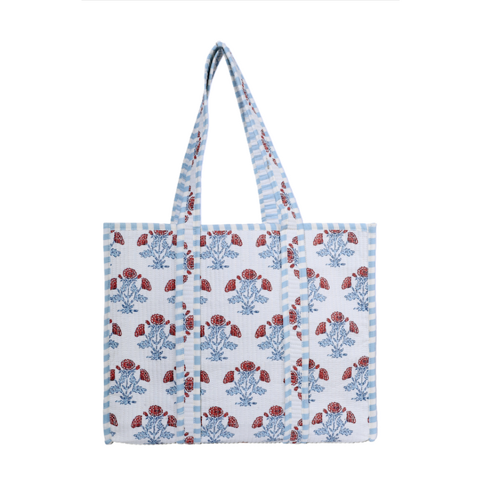 A white woven tote bag with blue and red floral block prints and blue-and-white striped handles, shown against a plain white background.
