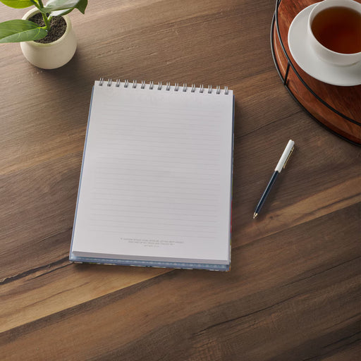 Notebook with pen on a wooden table with a cup of tea and plant.