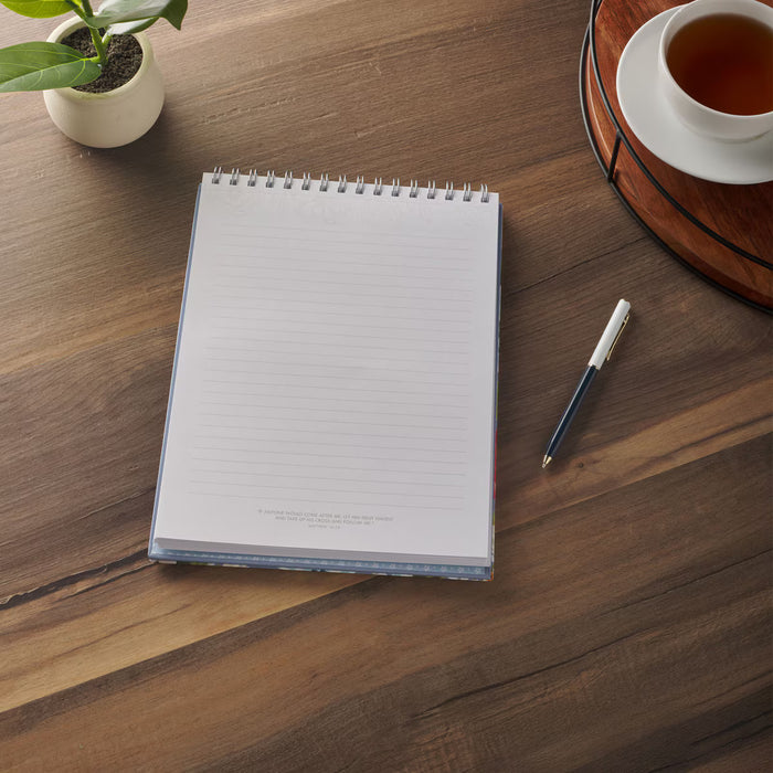 Notebook with pen on a wooden table with a cup of tea and plant.