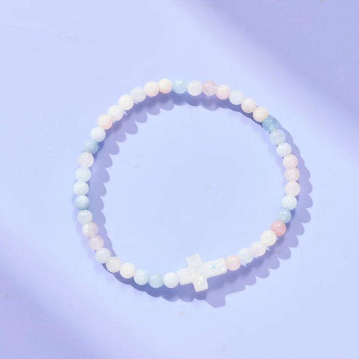 Beaded bracelet with a cross charm on a light purple background