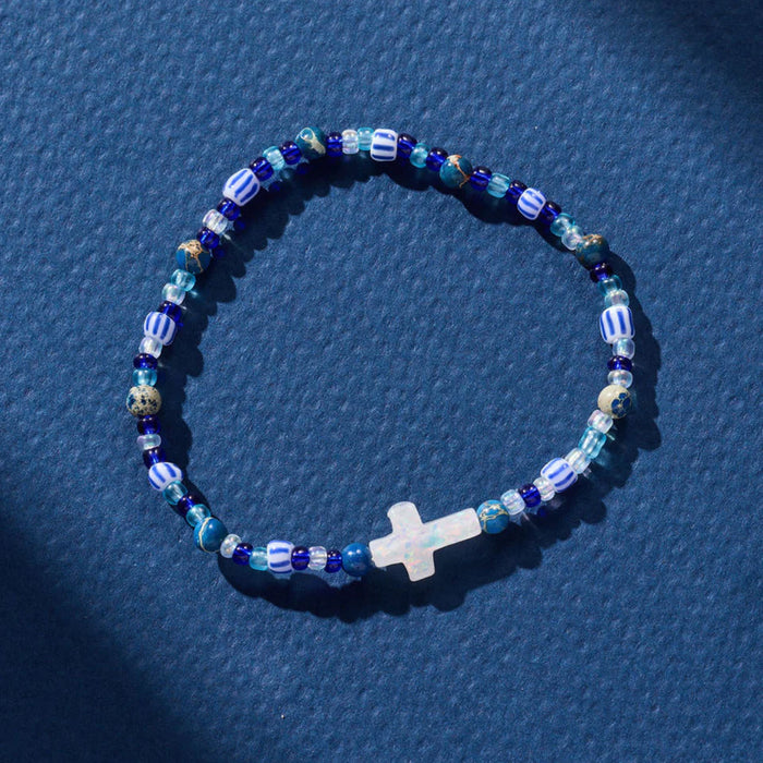 Beaded bracelet with a cross charm on a blue textured background