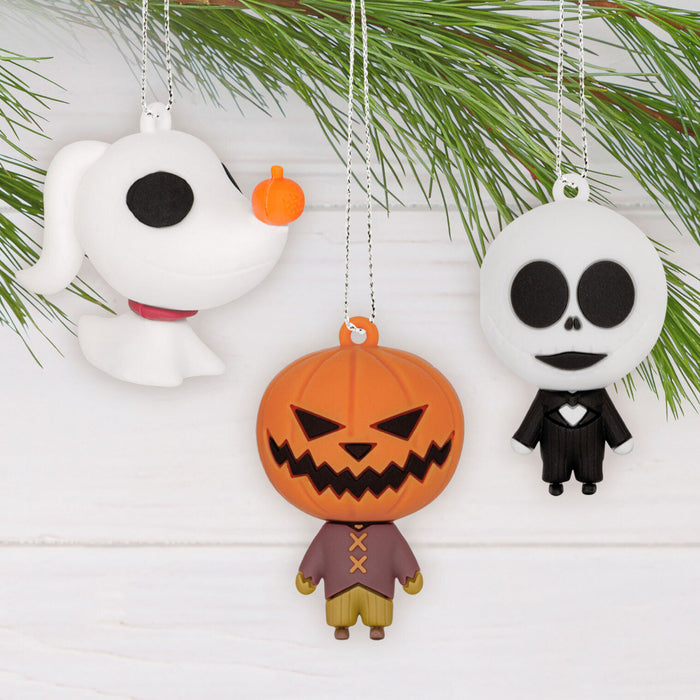 Halloween-themed ornaments including a ghost, jack-o'-lantern, and skeleton on a white background with greenery.