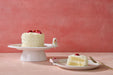 White cake with strawberries on a pink stand and plate against a pink background