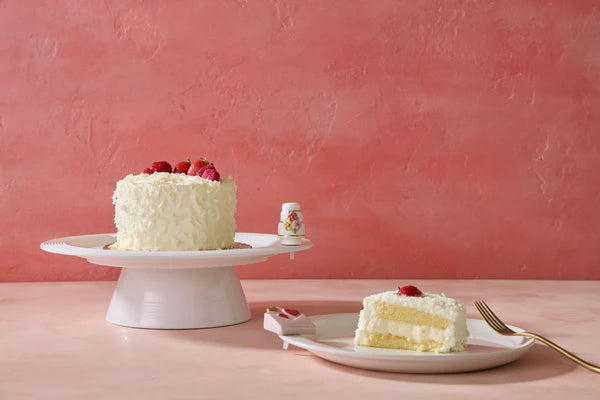 White cake with strawberries on a pink stand and plate against a pink background