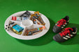 Snack tray with various bars and a soccer ball next to soccer cleats on a green background