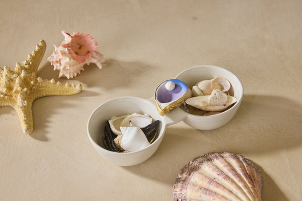 Two white ceramic bowls with seashells on a sandy background