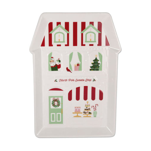 A white ceramic house-shaped serving platter featuring a Christmas-themed North Pole Sweets Shop design with red and green stripes, Santa, a Christmas tree, and candy canes, on a white background.