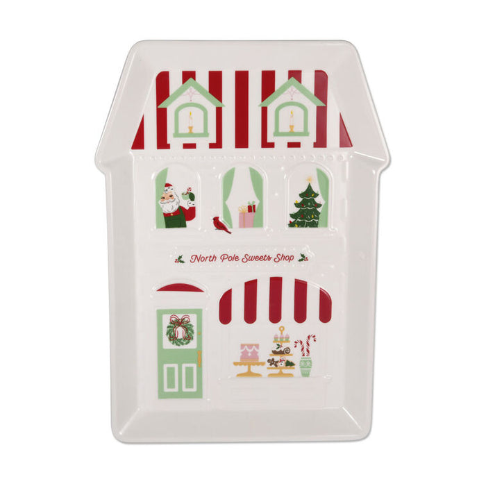 A white ceramic house-shaped serving platter featuring a Christmas-themed North Pole Sweets Shop design with red and green stripes, Santa, a Christmas tree, and candy canes, on a white background.