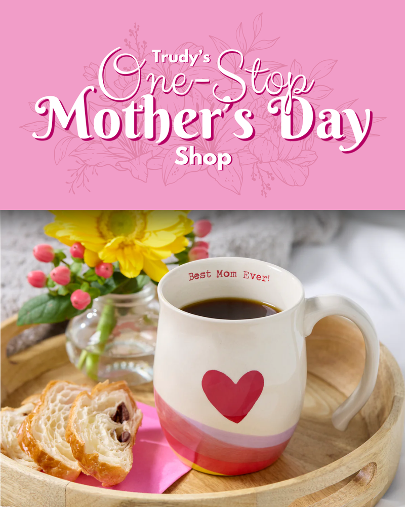 Mug with heart design, flowers, and bread on a tray against a pink background with 'Trudy's One-Stop Mother's Day Shop' text.