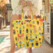 Person holding a yellow tote bag with insect pattern outdoors.