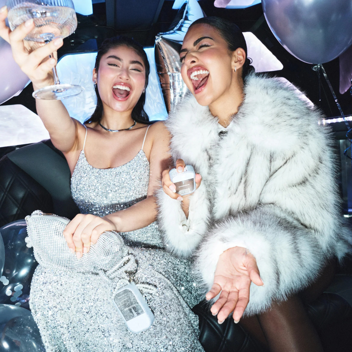 Two women celebrating inside a limousine with balloons and drinks.