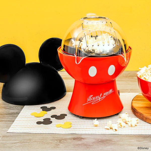 Red popcorn maker shaped like a Mickey Mouse head with popcorn and a bowl on a yellow background