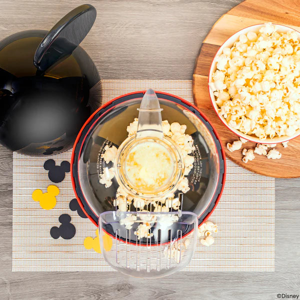 Popcorn maker with popcorn on a wooden board, next to a bowl of popcorn and Disney-themed cutouts.