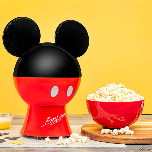 Red and black popcorn maker shaped like Mickey Mouse with a bowl of popcorn on a yellow background