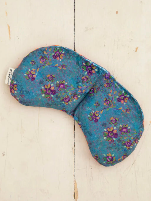 Blue floral-patterned eye pillow on a light wooden surface