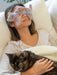 Woman with a floral eye mask holding a cat on a couch