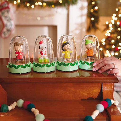 Four small figurines in glass domes on a wooden surface with a festive background.