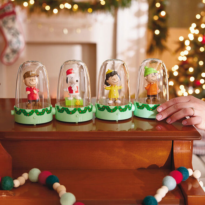Four small figurines in glass domes on a wooden surface with a festive background.