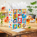 Colorful gift bag with cartoon characters on a wooden table with drinks and snacks.