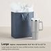 Gray gift bag with white tissue paper and a matching mug on a beige background