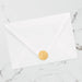 White envelope with a gold crown-shaped wax seal on a marble surface