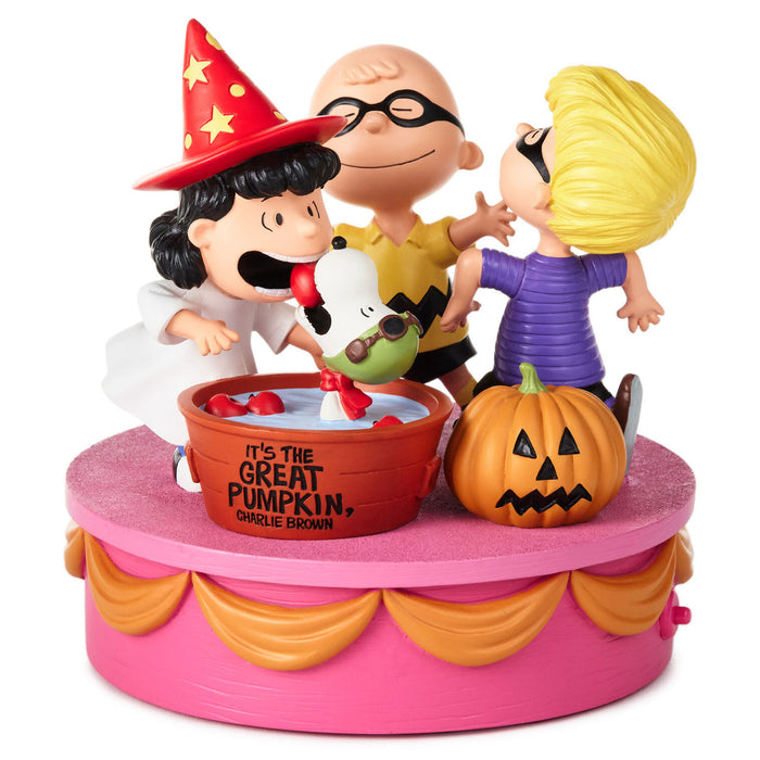 A Peanuts Halloween-themed collectible figurine set on a pink round base. The scene shows Charlie Brown in a wizard hat, Lucy in a purple dress, Snoopy, and a jack-o'-lantern pumpkin, with a red bucket labeled 'IT'S THE GREAT PUMPKIN, CHARLE BROWN' in the center.