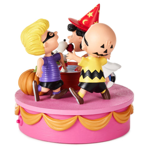 A collectible figurine of the Peanuts characters Charlie Brown, Snoopy, and Woodstock celebrating Halloween on a pink and gold cake-shaped base.