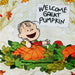 A close-up of a printed textile featuring Charlie Brown holding a sign that reads “WELCOME GREAT PUMPKIN,” surrounded by orange pumpkins and green leaves on a light cream background.