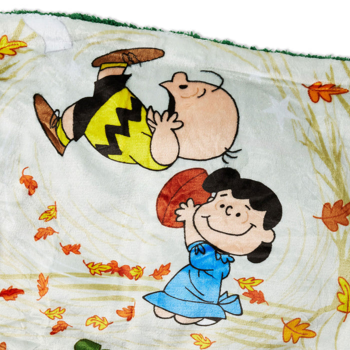A close-up of a printed fabric featuring Peanuts characters Charlie Brown and Lucy in an autumn outdoor scene with falling leaves.