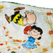 A close-up of a printed fabric featuring Peanuts characters Charlie Brown and Lucy in an autumn outdoor scene with falling leaves.