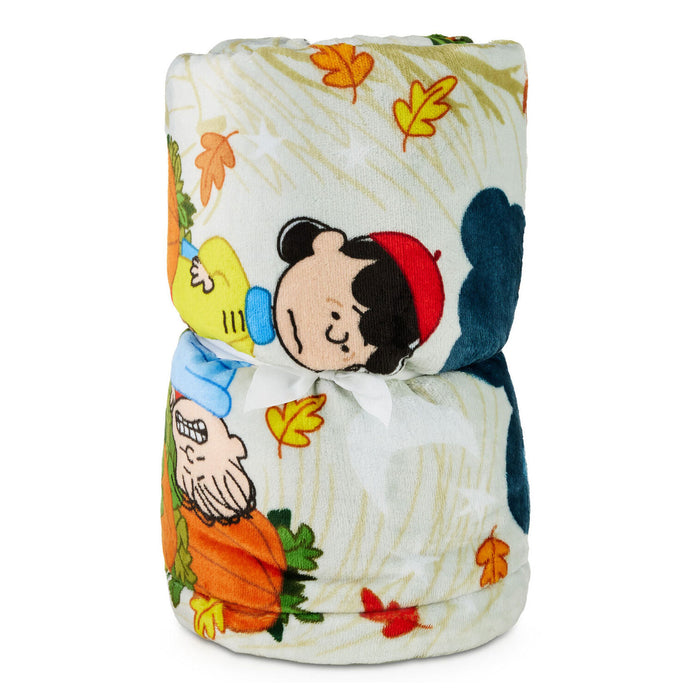 A folded plush blanket featuring a Peanuts autumn-themed print with Charlie Brown, Snoopy, pumpkins, and fall leaves on a cream background.