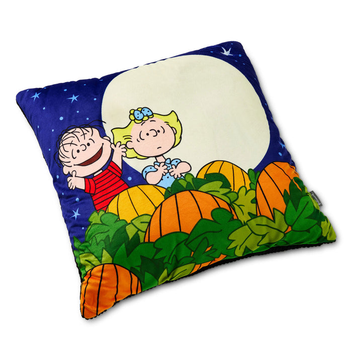 A square decorative pillow featuring a colorful Peanuts Halloween design with Charlie Brown and Snoopy in a pumpkin patch under a full moon.