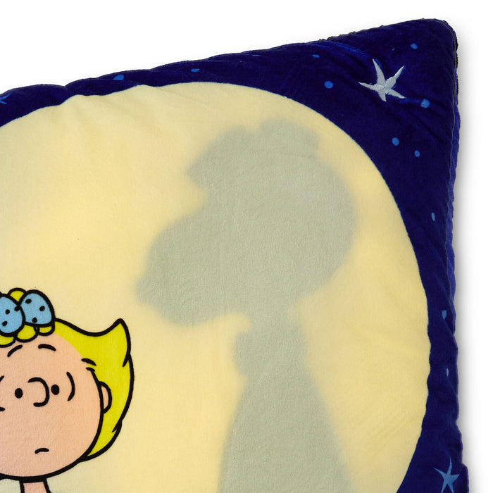 A close-up of a plush throw pillow featuring a dark blue border with white star details and a light cream center, printed with a cartoon character and a large cast shadow on the front.