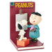 Figurine of a cartoon character painting a dog with a 'Peanuts' comic book in the background