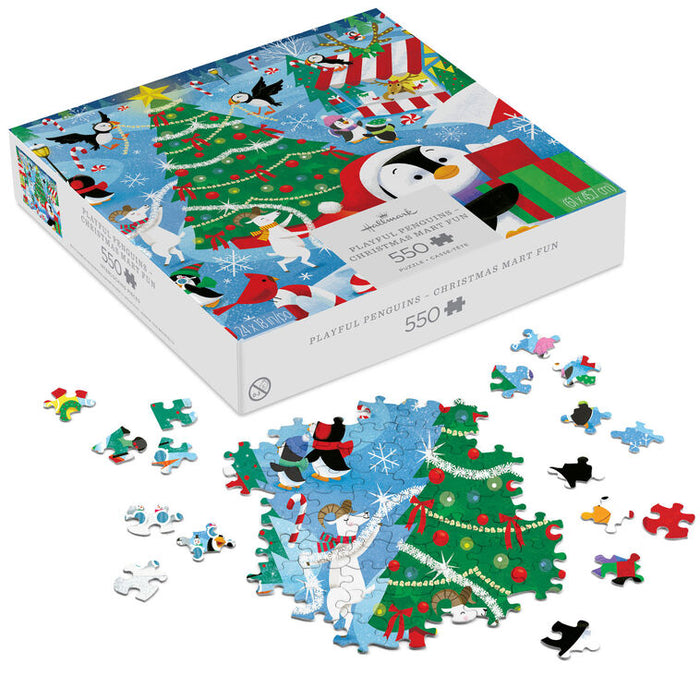 A 550-piece jigsaw puzzle box labeled 'Playful Penguins - Christmas Mart Fun' shown open with several loose puzzle pieces scattered in front. The box and assembled pieces feature a colorful winter holiday scene with penguins, a Christmas tree, snow, and festive decorations.