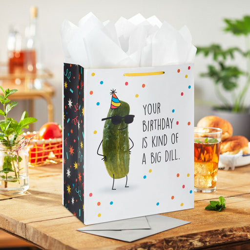 Gift bag with a pickle illustration and humorous birthday message on a table.