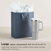 Gray gift bag with white tissue paper and a gray mug on a beige background