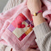 Pink robe with heart pattern held by a person wearing a heart-themed bracelet.