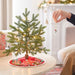 Small decorated Christmas tree on a table with a person's hand placing a ornament.