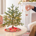 Person decorating a small Christmas tree with a butterfly ornament in a cozy living room.